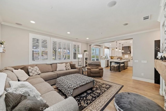 living room featuring light wood-style floors, visible vents, crown molding, and baseboards