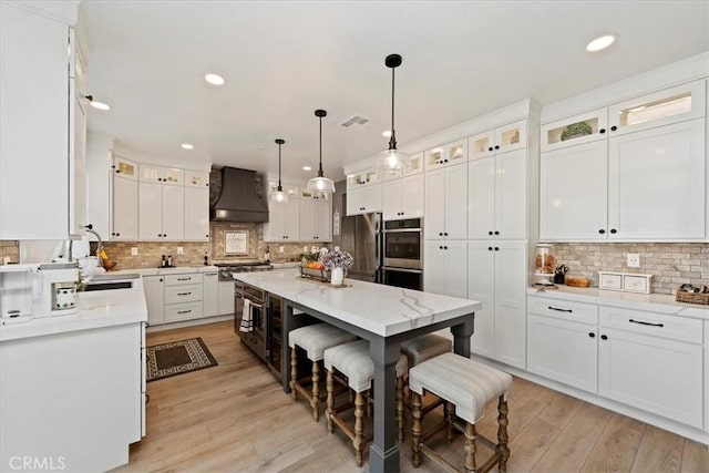 kitchen with a breakfast bar area, custom range hood, appliances with stainless steel finishes, white cabinetry, and a sink