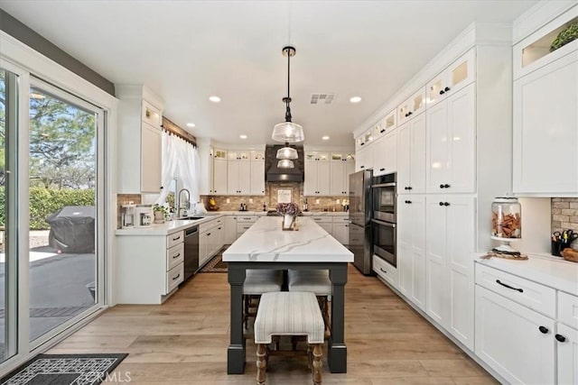 kitchen with a sink, visible vents, white cabinets, stainless steel dishwasher, and custom exhaust hood