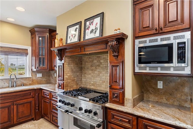 kitchen with glass insert cabinets, light stone counters, decorative backsplash, stainless steel appliances, and a sink