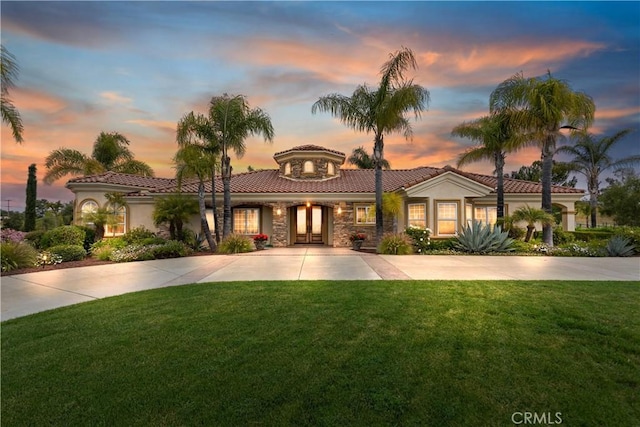 mediterranean / spanish home with concrete driveway, a lawn, french doors, stucco siding, and stone siding