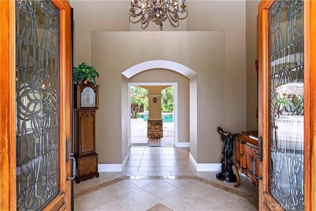 entryway with an inviting chandelier, light tile patterned flooring, baseboards, and arched walkways