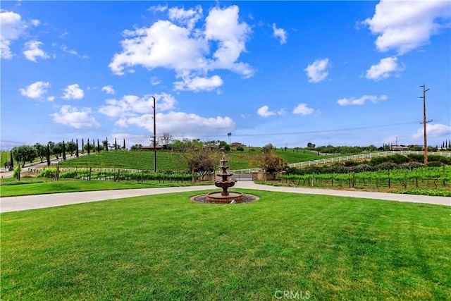 view of community featuring a rural view, a lawn, and fence