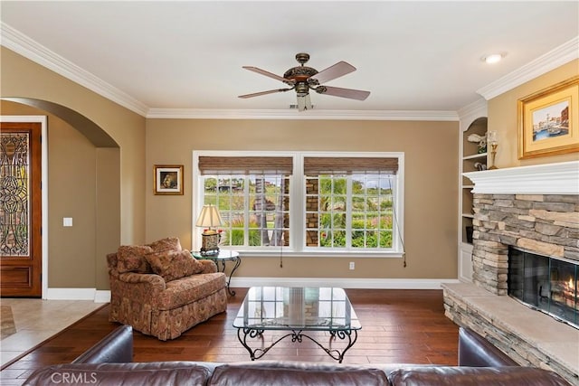 living room with hardwood / wood-style flooring, arched walkways, a stone fireplace, crown molding, and baseboards