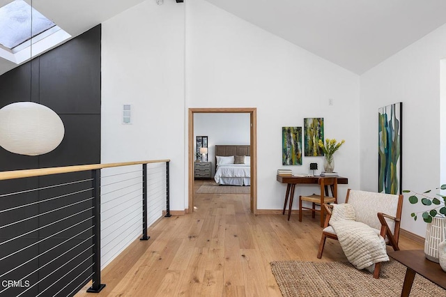 hall featuring light wood-style floors, a skylight, high vaulted ceiling, and baseboards