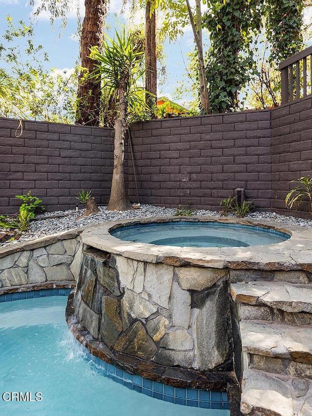 view of swimming pool featuring an in ground hot tub and a fenced backyard