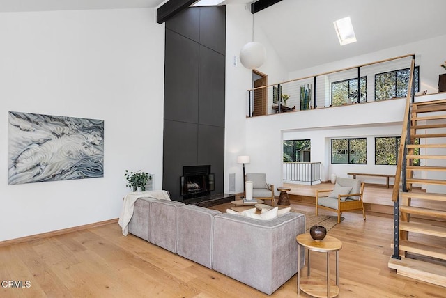 living room with a skylight, baseboards, stairway, light wood-style floors, and beam ceiling