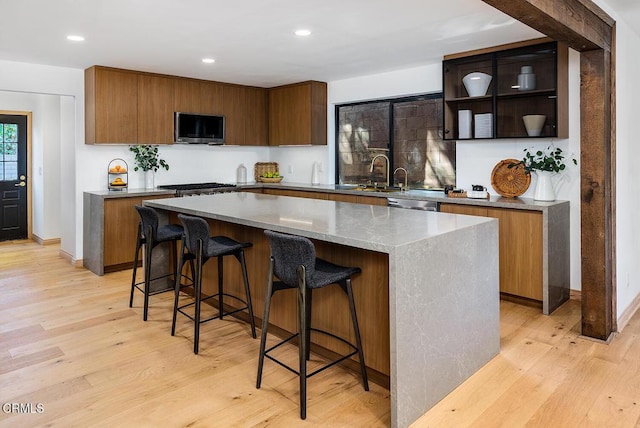 kitchen with a center island, open shelves, light wood-style flooring, stainless steel dishwasher, and a kitchen bar