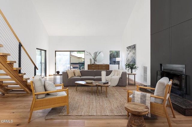 living area featuring high vaulted ceiling, visible vents, a fireplace, and light wood finished floors