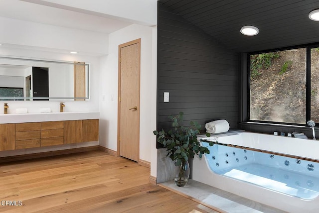 bathroom with wooden walls, wood ceiling, wood finished floors, a jetted tub, and vanity