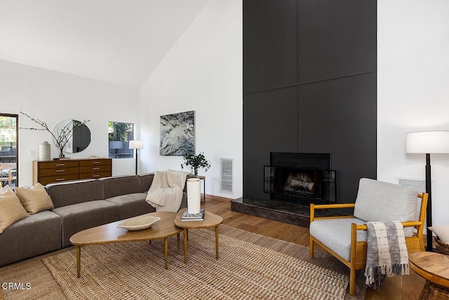 living area with a large fireplace, high vaulted ceiling, light wood-style flooring, and visible vents