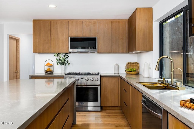 kitchen with brown cabinetry, stainless steel appliances, light wood-type flooring, a sink, and recessed lighting