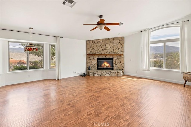 unfurnished living room featuring baseboards, visible vents, a ceiling fan, wood finished floors, and a stone fireplace