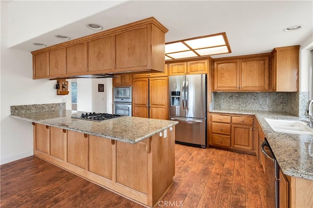 kitchen featuring stainless steel appliances, wood-type flooring, a sink, and a peninsula