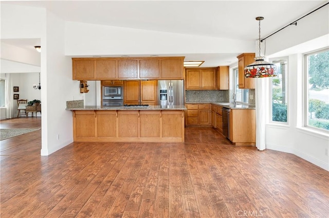 kitchen featuring appliances with stainless steel finishes, backsplash, a peninsula, and hardwood / wood-style flooring