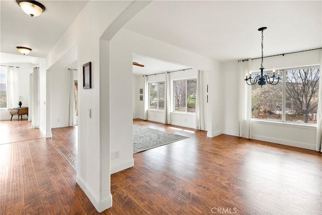 unfurnished dining area featuring arched walkways, wood-type flooring, baseboards, and a notable chandelier