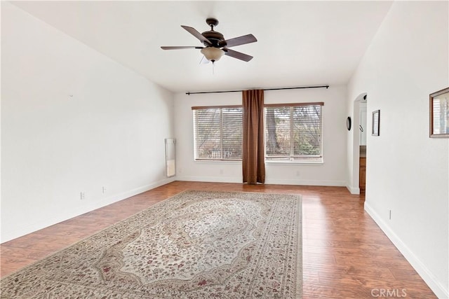 unfurnished room featuring arched walkways, ceiling fan, wood finished floors, and baseboards