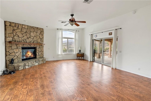 unfurnished living room with a stone fireplace, wood finished floors, a ceiling fan, and a healthy amount of sunlight