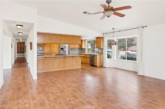 kitchen featuring lofted ceiling, stainless steel appliances, light countertops, decorative backsplash, and light wood finished floors