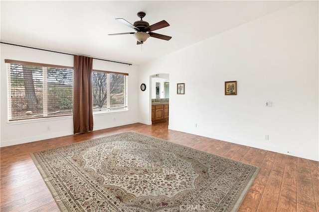 unfurnished room with arched walkways, baseboards, lofted ceiling, wood-type flooring, and ceiling fan