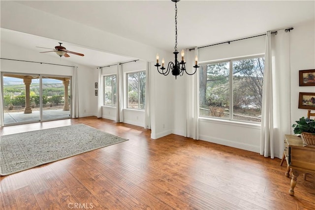 unfurnished dining area with ceiling fan with notable chandelier, lofted ceiling, baseboards, and wood finished floors