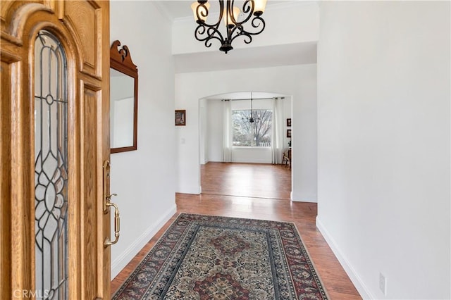 corridor with a chandelier, arched walkways, dark wood-style flooring, baseboards, and ornamental molding