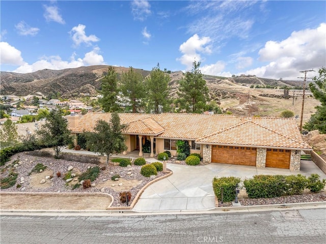 ranch-style home featuring concrete driveway, stone siding, a tiled roof, an attached garage, and a mountain view