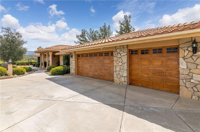 mediterranean / spanish-style house with a garage, driveway, stone siding, and a tile roof