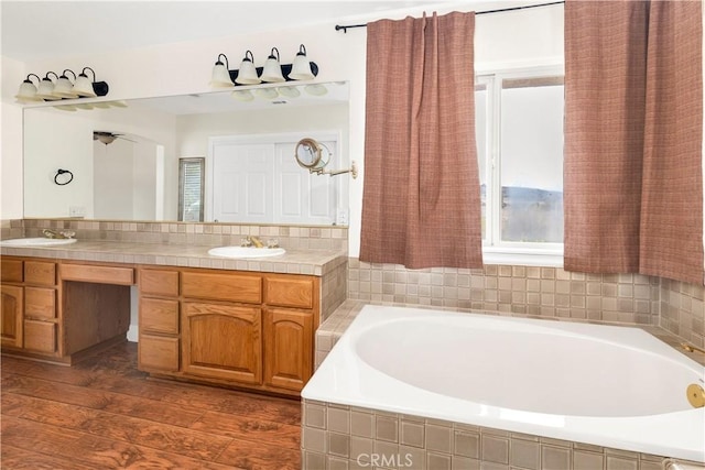 full bath with a garden tub, double vanity, wood finished floors, and a sink