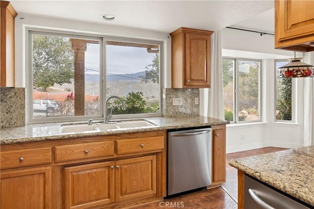 kitchen with light stone counters, a sink, decorative backsplash, dishwasher, and brown cabinetry