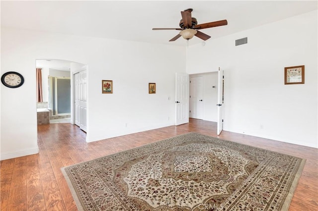 empty room featuring a ceiling fan, arched walkways, visible vents, and wood finished floors