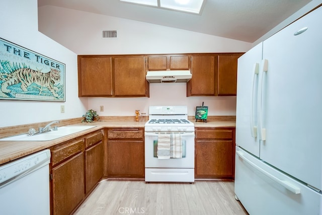 kitchen with brown cabinetry, vaulted ceiling, a sink, white appliances, and under cabinet range hood