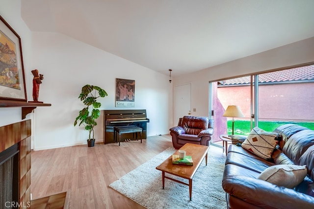 living room featuring vaulted ceiling, a fireplace, light wood-style flooring, and baseboards