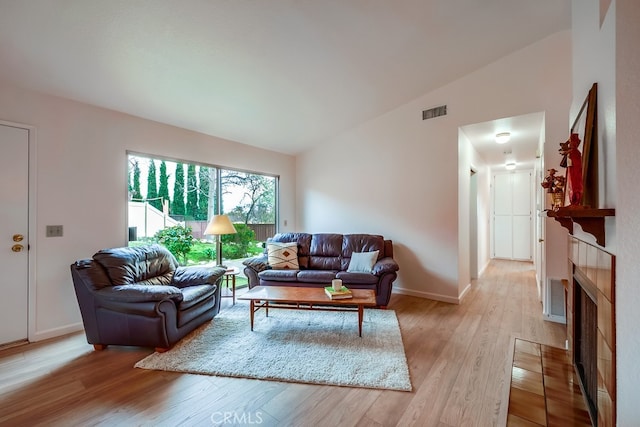 living room featuring visible vents, a tiled fireplace, light wood-style floors, vaulted ceiling, and baseboards