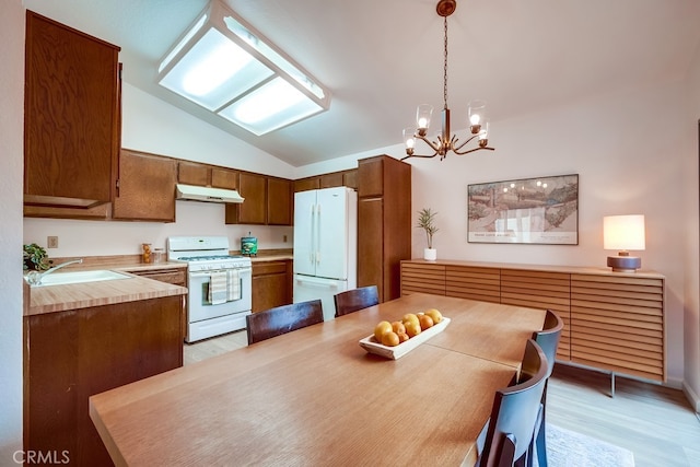 kitchen featuring light wood finished floors, lofted ceiling, light countertops, white appliances, and under cabinet range hood