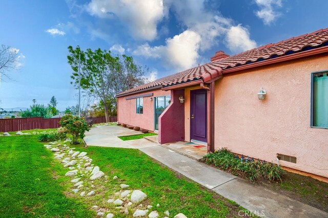 view of exterior entry with a chimney, fence, a tile roof, and stucco siding