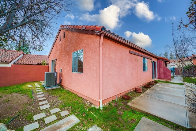 view of side of home featuring central AC unit, a tile roof, fence, a patio area, and stucco siding