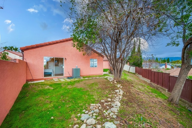 rear view of property featuring cooling unit, a fenced backyard, a yard, and stucco siding