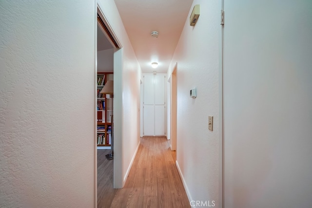 hallway with light wood-style floors, a textured wall, and baseboards