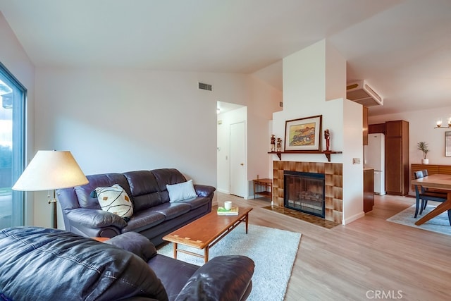 living room featuring visible vents, a tiled fireplace, vaulted ceiling, light wood-style floors, and a notable chandelier