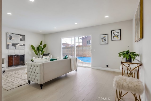 living area featuring a brick fireplace, light wood-style flooring, baseboards, and recessed lighting