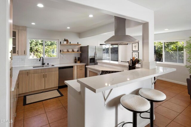 kitchen featuring a breakfast bar area, light tile patterned flooring, stainless steel appliances, a sink, and island exhaust hood