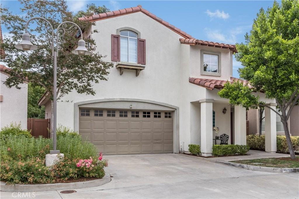 mediterranean / spanish home featuring fence, stucco siding, concrete driveway, a garage, and a tiled roof