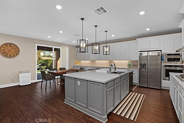 kitchen featuring a center island with sink, visible vents, dark wood-style flooring, stainless steel appliances, and gray cabinetry