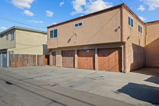 rear view of property with an attached garage, fence, and stucco siding