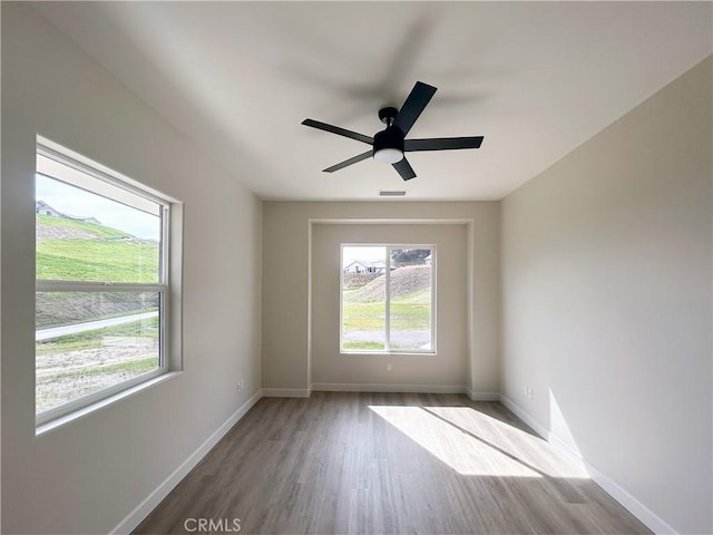 spare room featuring visible vents, ceiling fan, baseboards, and wood finished floors