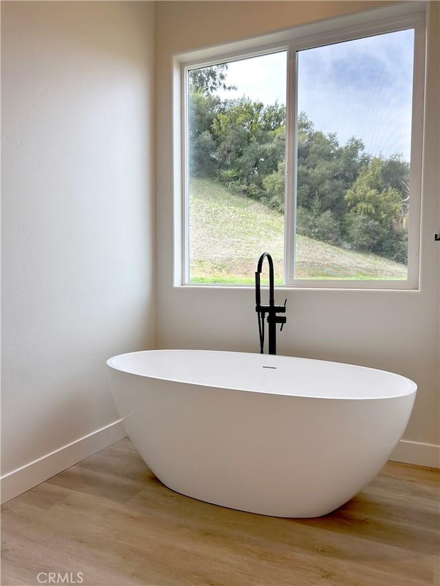 bathroom with a freestanding tub, wood finished floors, and baseboards