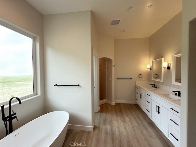 bathroom with a freestanding tub, wood finished floors, a sink, visible vents, and baseboards