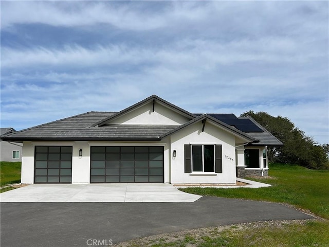 view of front of house featuring a garage, a front yard, concrete driveway, roof mounted solar panels, and stucco siding