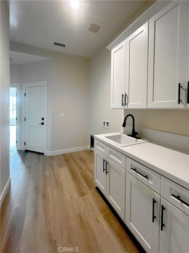 kitchen with visible vents, light wood-style flooring, white cabinetry, a sink, and baseboards